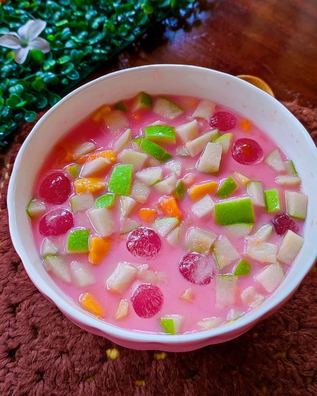 A bowl of pink dessert soup with colorful fruit and vegetables.